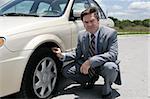 An unhappy looking businessman discovering a screw in his flat tire.