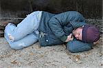 A homeless man sleeping on the ground beside a dumpster.