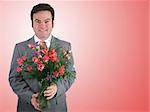 A handsome husband in a suit holding a bouquet of pink sweetheart roses over a pink packground.