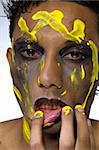 Studio portrait of mixed race young man smearing yellow paint all over his face