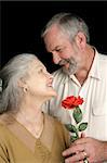 A handsome mature husband surprising his wife with a red rose.  Vertical view over black.