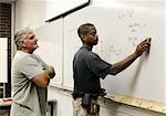 A teacher looks on as his adult education student erases the board.