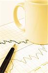 Pen and cup on Forex candlestick chart in yellow lighting