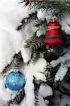 Christmas ornaments hanging on snow covered spruce tree outside