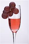 A glass of rose wine with grapes against a plain background.