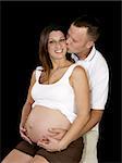 Beautiful expectant mother receiving a kiss from her loving husband.  Black background.