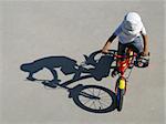 A little boy riding a bike with his shadow on a gray background