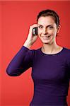 A casual portrait of a brunette caucasian female talking on a cell phone with a red background