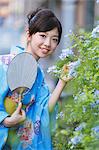 Young Woman Dressed In Yukata Standing By Flower Plants