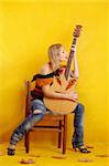 woman with guitar, sitting on a cheir, isolated on yellow