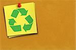 green recycling symbol on yellow note against cardboard background