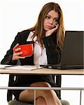 Attractive young brunette woman in business suit looking bored while looking at a computer screen while holding a red coffee mug