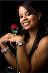 Beautiful young African American woman holding a red rose near face smiling on black background