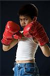 Young asian boy with serious expression wearing red boxing gloves standing on black background
