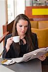 business woman relaxing in a bar drinking coffee and reading news paper
