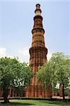 Looking through the trees at Qutub Minar, the red sandstone tower in Delhi, India, covered with beautiful carvings.