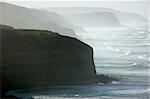 Rough waves batter the cliffs of a rugged coastline.