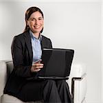 Caucasian mid adult professional business woman sitting in modern office working on laptop looking at viewer and smiling.