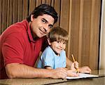Hispanic father and son smiling at viewer with homework.