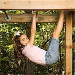 Side view of Hispanic girl hanging by arms and legs from monkey bars smiling at viewer.