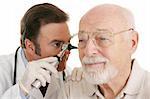 Doctor using otoscope to look in a senior man's ears.  Closeup on white.  Focus on doctor.