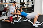 Man assisting woman at gym with hand weights smiling.