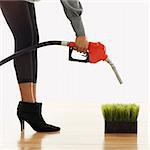 Woman holding gasoline pump nozzle over green grass.