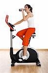 Young woman training on exercise bike at the gym and drinking water