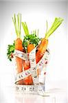 Carrots in a measuring cup with tape measure on white background