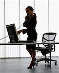 Silhouette of Caucasian businesswoman standing at computer  desk on telephone.