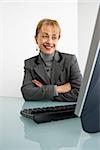 Caucasian woman looking at computer and smiling with arms crossed.