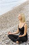A beautiful young blond woman sitting cross legged in a yoga position on a beach