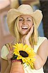 A beautiful young blond woman wearing a straw cowboy hat and smiling while carrying a shopping bag of sunflowers