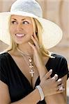 A classy, beautiful young blond woman wearing a sun hat , smiling and wearing a black dress and silver jewelry