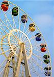 Big ferris wheel with colored cabins on cloudy sky