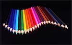 Colorful pencils arranged in a wave isolated over black background