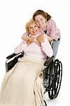 Senior woman in wheelchair gets hug from her teen granddaughter.  Isolated on white.