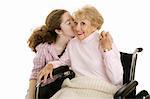 Senior woman smiles as she gets a kiss from her granddaughter.  Isolated on white.