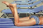 Legs of a girl in a stripped swimsuit laying on a stripped sun bed