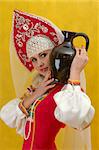 Close-up. Woman in a folk russian dress holds a jug on yellow background