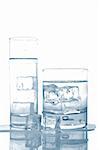 Two glasses of fresh mineral water with ice cubes reflected on wet background. Shallow depth of field
