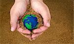 hands holding sand with small green and blue earth