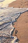 Tropical sandy beach with footprints and ocean wave