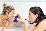 one blond girl and one brunette in the same bathtub playing with flowers