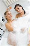 two cute girls togheter in a bathtub with foam looking and smiling