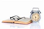 book with alarm clock and eyeglasses on white background