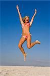 A beautiful young blond woman jumps high on a sandy beach