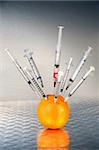 Syringes inserted into an orange against dark background