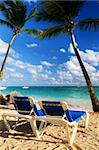 Sandy beach of tropical resort with palm trees and two reclining chairs