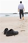 Businessman walking barefoot on a beach. Focus on his shoes in the foreground.